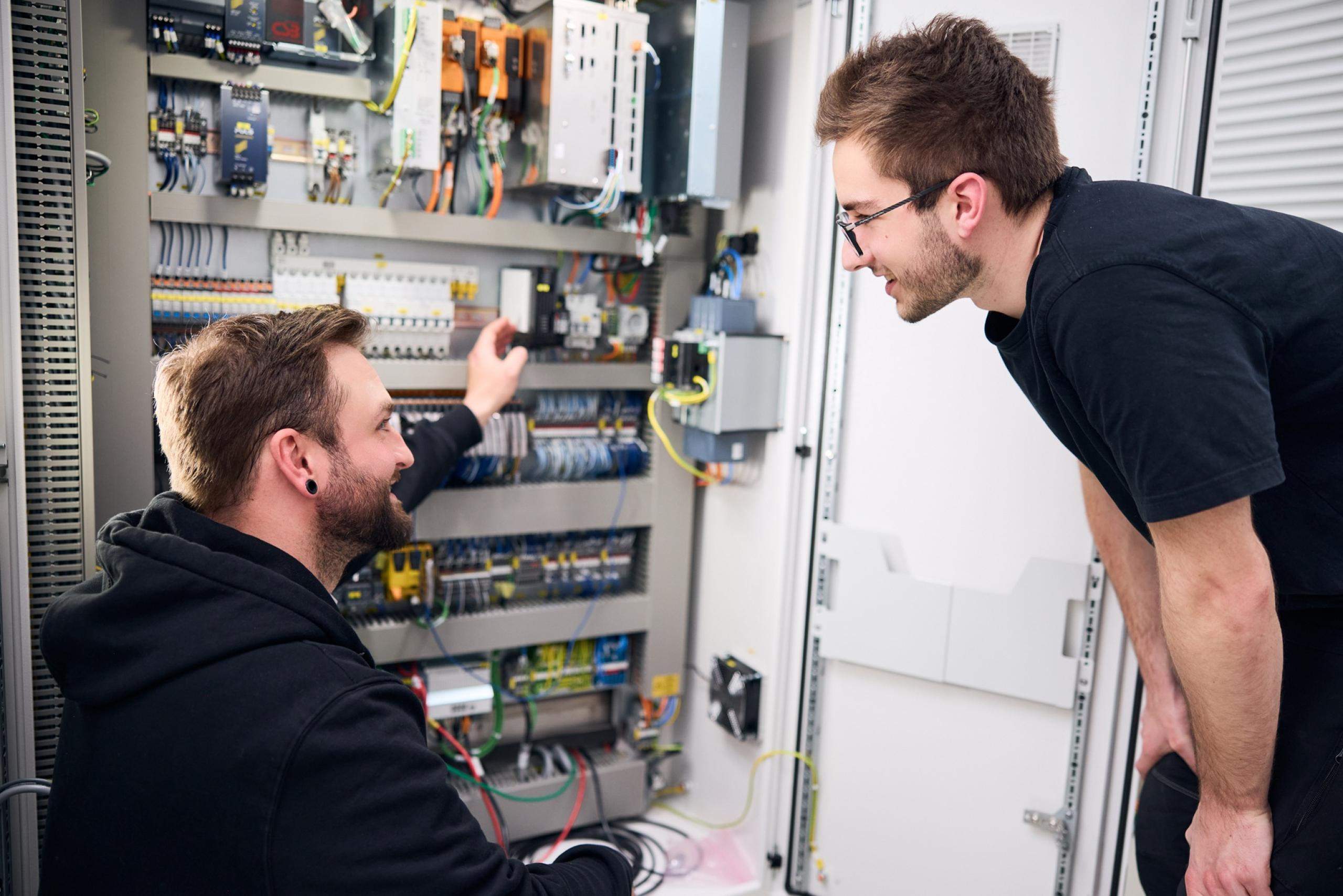Trainer with Mechatronics Trainee in Front of Open Control Cabinet